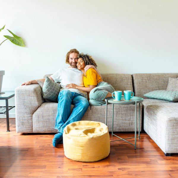 Cheerful multiracial couple sitting on sofa in the living room - Happy family moving in new home - Real estate and stylish furniture concept